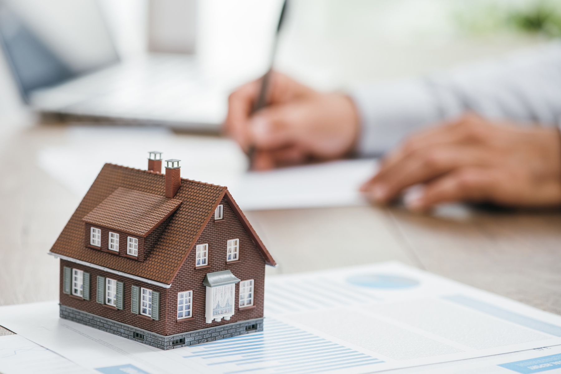 Real estate agent working in his office, he is writing a contract and house model on the foreground: investments, home loan and insurance concept